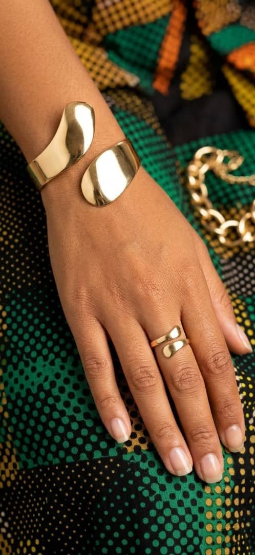 Ensemble bracelet et bague doré ajustable, style moderne, porté sur une main avec tissu coloré.